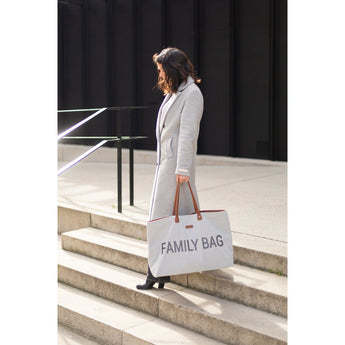 Woman in a grey coat carrying a large light grey "FAMILY BAG" tote with brown leather handles down concrete steps.