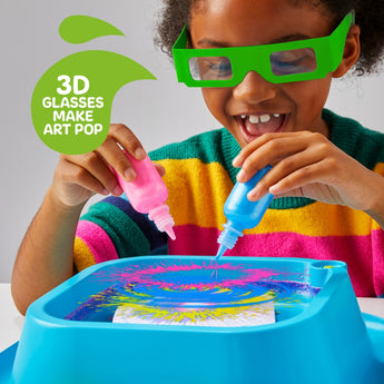 Smiling child in green 3D glasses creating vibrant neon spin art with pink and blue paints on a blue art station.