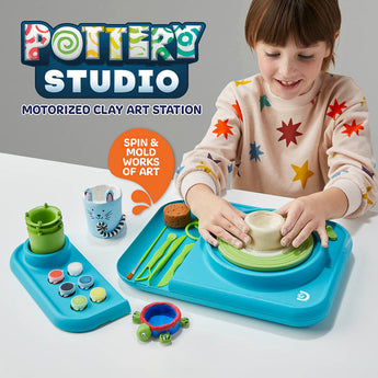 Child using a blue motorized pottery wheel studio with clay, tools, paints, and a finished cat-themed pot.