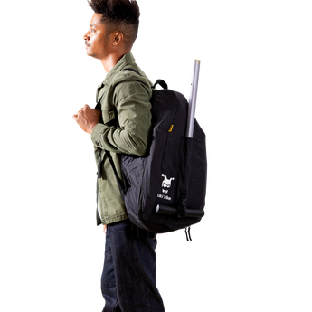 Man wearing a black Doona Liki Trike Travel Bag backpack with a trike handle extending from the top.