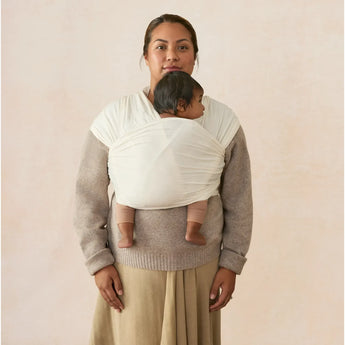 Woman wearing an Ergobaby Aura Sustainably Sourced Knit Baby Wrap in cream with a baby nestled inside.