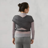 Woman from behind wearing a dark grey Ergobaby Aura knit baby wrap over a light grey top.