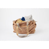 Ergobaby Aura knit baby wrap in grey stripes, folded inside a tan leather bag with other items.