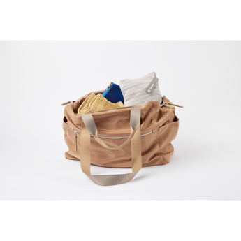 Ergobaby Aura knit baby wrap in grey stripes, folded inside a tan leather bag with other items.