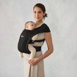 Woman wearing a black Ergobaby Embrace newborn carrier with a baby facing inward.