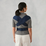 Woman from behind wearing a heather grey Ergobaby Embrace carrier with navy blue straps.