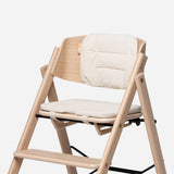 KAOS Klapp reversible highchair cushion set in cream, shown on a natural wood highchair.
