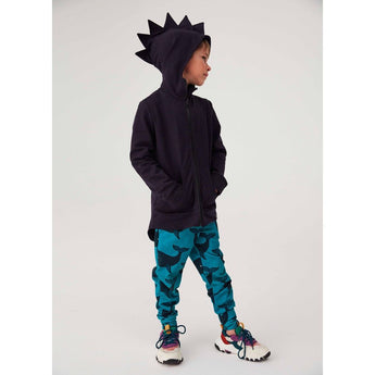 Boy wearing a navy Kuku Kid Dino Hoodie Cardigan Jacket with spiked hood and blue whale-print leggings.