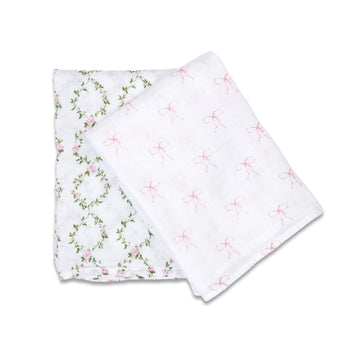 Two folded white cotton muslin swaddles: one with pink floral vines, one with pink bows.