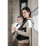 Woman in a cream sweater carrying a baby in a dark gray MiaMily Hipster ergonomic baby carrier.