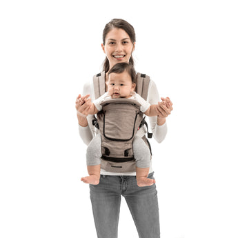 Smiling parent wearing a beige MiaMily Hipster ergonomic baby carrier with a baby facing forward.