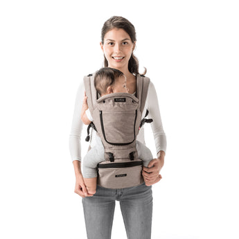 Smiling parent wearing a beige MiaMily Hipster ergonomic baby carrier with a baby facing forward.