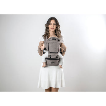 Woman in white dress carrying baby in a gray MiaMily Hipster ergonomic baby carrier with hip seat.