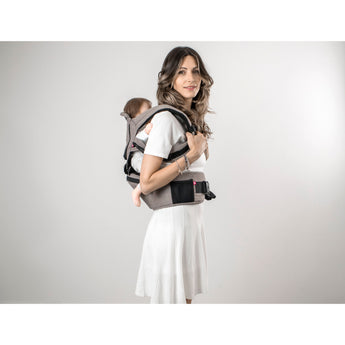 Woman wearing a gray MiaMily Hipster ergonomic baby carrier with a baby on her back.