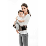 Smiling mom holds baby in a brown MiaMily Hipster ergonomic baby carrier with hip seat.