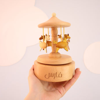 Personalized light wood music carousel with three horses, engraved with "فارس" on the base.