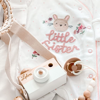 Personalized wooden camera toy with "Lulwa" engraving, white and natural wood, on a "Little Sister" bunny onesie.