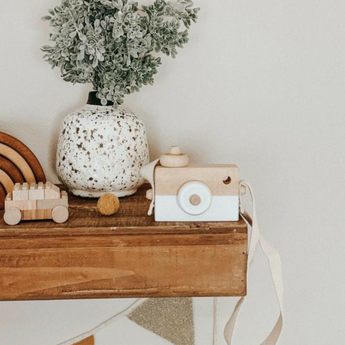 Personalized wooden camera toy with a white lens, natural wood body, and strap, on a wooden shelf.