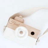 Personalized wooden camera toy with "Harib" engraved, natural wood and white paint, cream strap.