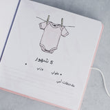 Open pink suede baby milestone album page with "Daddy Love" onesie illustration and Arabic text.