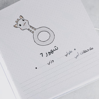 White baby milestone album page with a giraffe illustration and Arabic text for "7 months," "My notes," "height," and "weight.