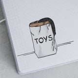 Hand-drawn illustration of a white paper bag labeled "TOYS" with a black polka-dot fabric peeking out, on a grid notebook page.