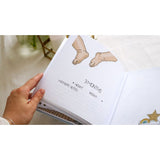 Hand holding open a personalized baby milestones photo album with "3 Months" page, baby feet illustration, and dotted lines.
