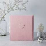 Pink suede baby milestones photo album with embossed heart, tied with white ribbon.