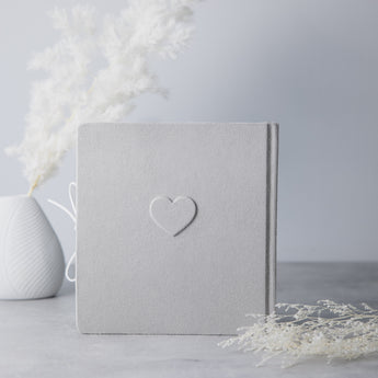 Light gray suede baby milestone photo album with an embossed heart and white ribbon tie.