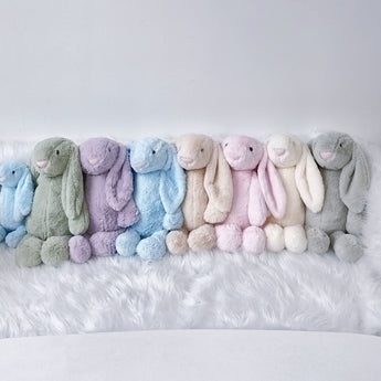 Row of soft, plush bunny toys in pastel colors: blue, green, purple, light blue, beige, pink, cream, and grey.