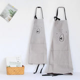 Two light gray kids' aprons with black bear face designs and black straps, one smaller, hanging on a white wall.