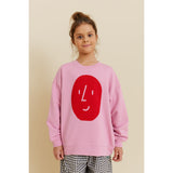 Girl in an oversized pink organic cotton sweatshirt with a red "potato face" print, paired with checkered pants.