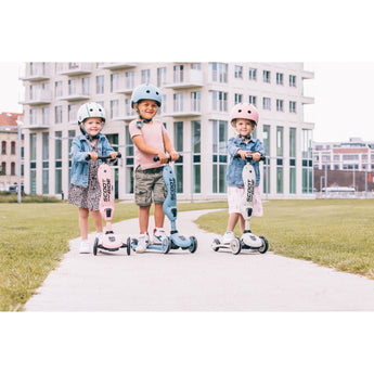 Three children with helmets on Scoot & Ride Highwaykick 1 scooters in pink, blue, and white.