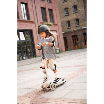 Child in helmet and pads riding a beige Scoot & Ride Highwaykick 3S LED 3-wheel light-up scooter.