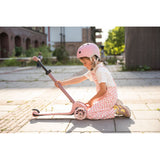 Girl in pink helmet and checkered overalls adjusting a pink Scoot & Ride Highwaykick 3S LED 3-wheel scooter.