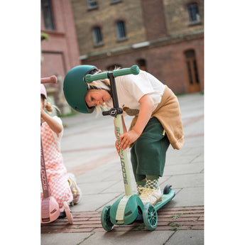 Child in green helmet adjusts a mint green Scoot & Ride Highwaykick 3S LED 3-wheel scooter.
