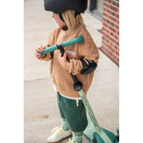 Young child in helmet and elbow pads adjusting a green Scoot & Ride Highwaykick 3S LED scooter.