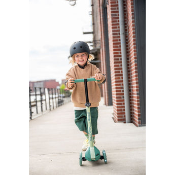 Smiling child in a helmet riding a green Scoot & Ride Highwaykick 3S LED 3-wheel light-up scooter.