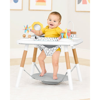 Happy baby in Skip Hop Discoverosity 3 Stage Activity Center with white frame, wooden legs, and colorful toys.