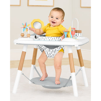 Happy baby in a white and wood Skip Hop Discoverosity 3 Stage Activity Center with colorful toys.