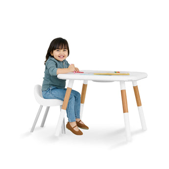Smiling child at a white Skip Hop activity table with natural wood legs and matching chair.