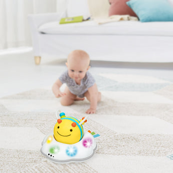 Yellow and white Skip Hop Follow Bee crawl toy with colorful lights on a rug, with a baby crawling in the background.