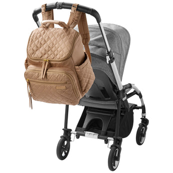 Tan quilted Skip Hop Forma backpack nappy bag hanging on a gray stroller handle.