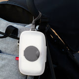 White Skip Hop Grab & Go Wipes Case with gray seal and strap, hanging from a black stroller handle.