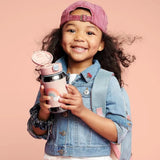 Smiling child holding a pink Skip Hop stainless steel straw water bottle with a rainbow design.