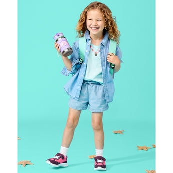 Smiling child holding a purple Skip Hop stainless steel straw water bottle with a seashell design.