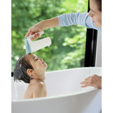 Mom uses a white and light blue Skip Hop Moby Waterfall Rinser to rinse a happy child's hair in a white bathtub.