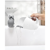 White Skip Hop Moby whale rinser with grey rubber lip pouring water into a white bathtub.
