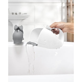 White Skip Hop Moby whale rinser with grey rubber lip pouring water into a white bathtub.