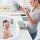 Smiling baby in a white tub, happy mom holding a gray Skip Hop Moby Waterfall Rinser with a soft lip.
